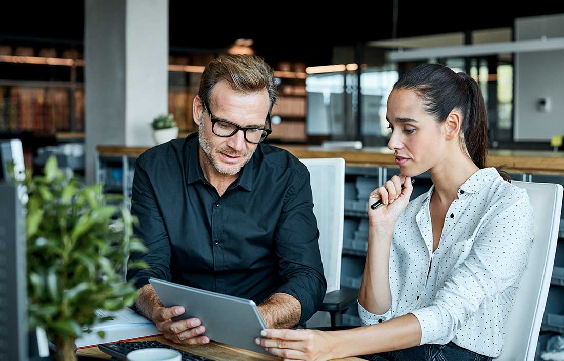 Two people sitting at a desk looking at a tablet of equity market data