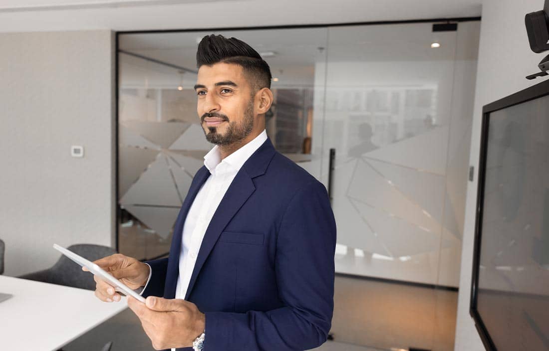 Man in a suit holding a tablet and looking to the side.