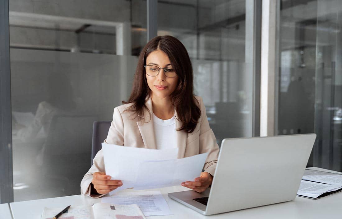 Woman looking down at a piece of paper with her laptop open.