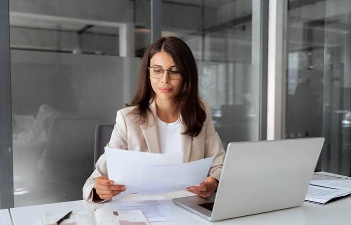 Woman looking down at a piece of paper with her laptop open.