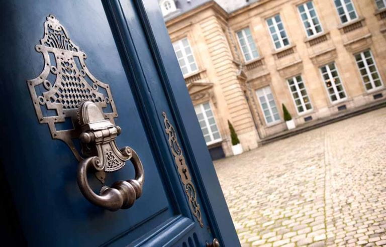 Opened door with a brass dorr knocker with view of a historic building.