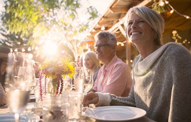 A family is sitting outdoors at a table smiling and eating.