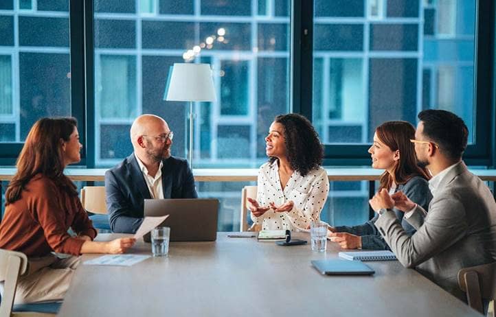 Business professionals sitting at a conference room table discussing with one another